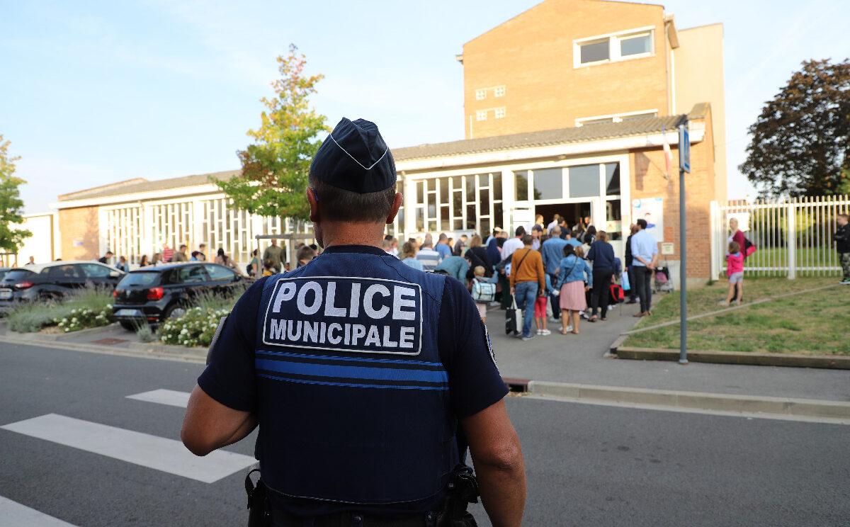 image représentant un policier municipal de dos surveillant une sortie d'école