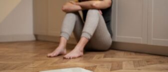 Image représentant une femme assise contre un mur recroquevillée devant une balance