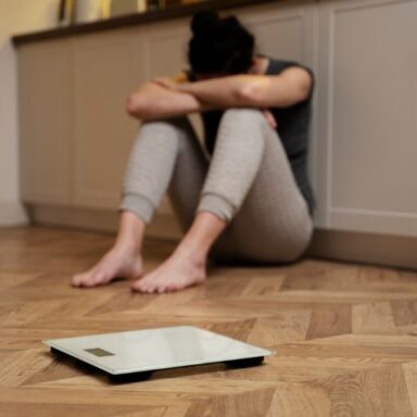 Image représentant une femme assise contre un mur recroquevillée devant une balance