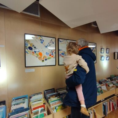 Image d'une personne de dos portant un enfant devant une exposition à la médiathèque Marguerite Yourcenar